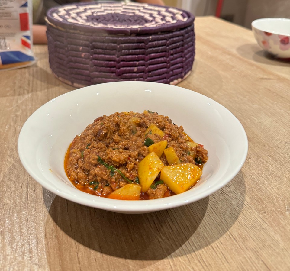 A white bowl of aaloo qeema with tender potato chunks and savoury mince on a kitchen table
